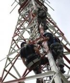Telecommunications workers climb up the metal framework of an antenna